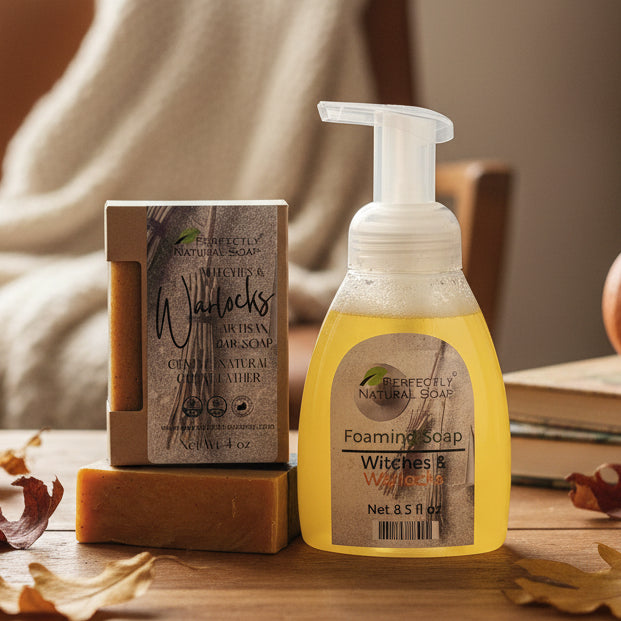 A bottle of Perfectly Natural Soaps Witches & Warlocks foaming soap with yellow liquid, standing next to its kraft paper box on a wooden block in front of a white subway tile wall.