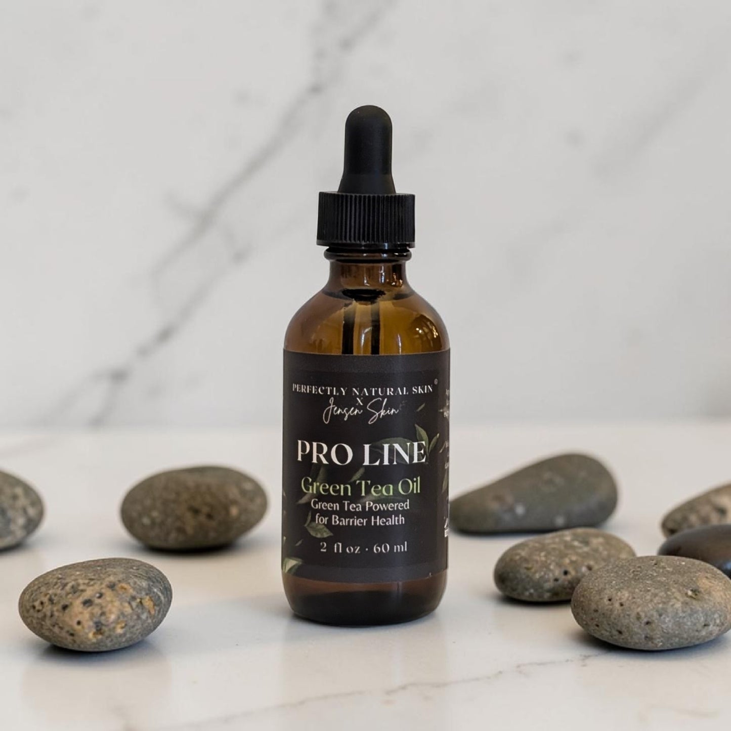 Bottle of Pro Line Green Tea Oil with a dropper on a marble surface with stones.