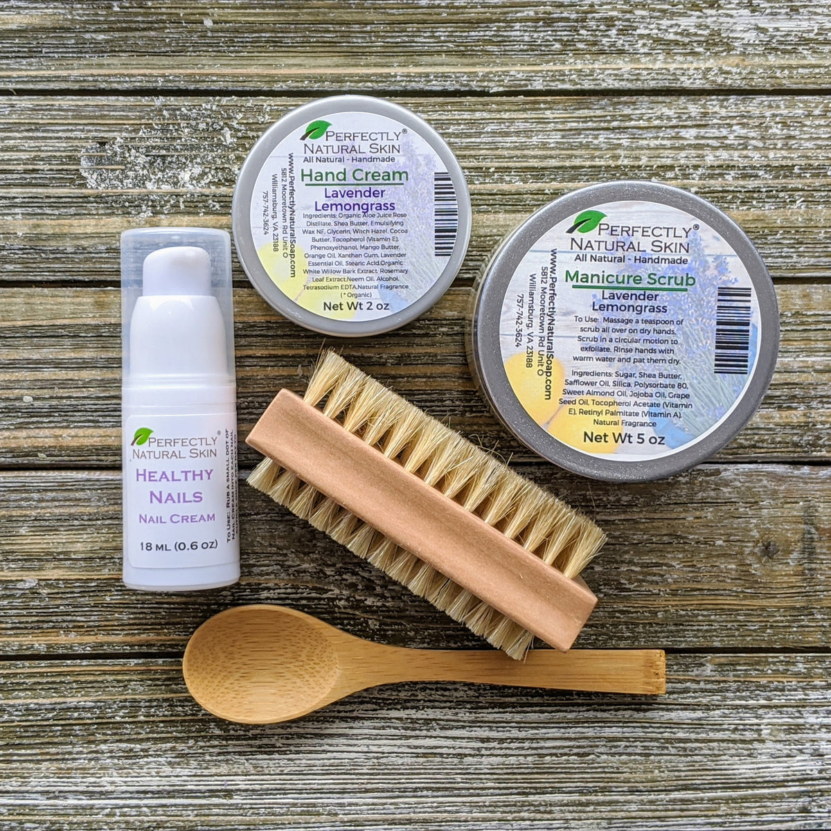 A flat-lay of Perfectly Natural Skin manicure and hand care products on a rustic wood background, including a hand cream jar, a manicure scrub tin, a nail cream tube, a wooden brush, and a wooden spoon.