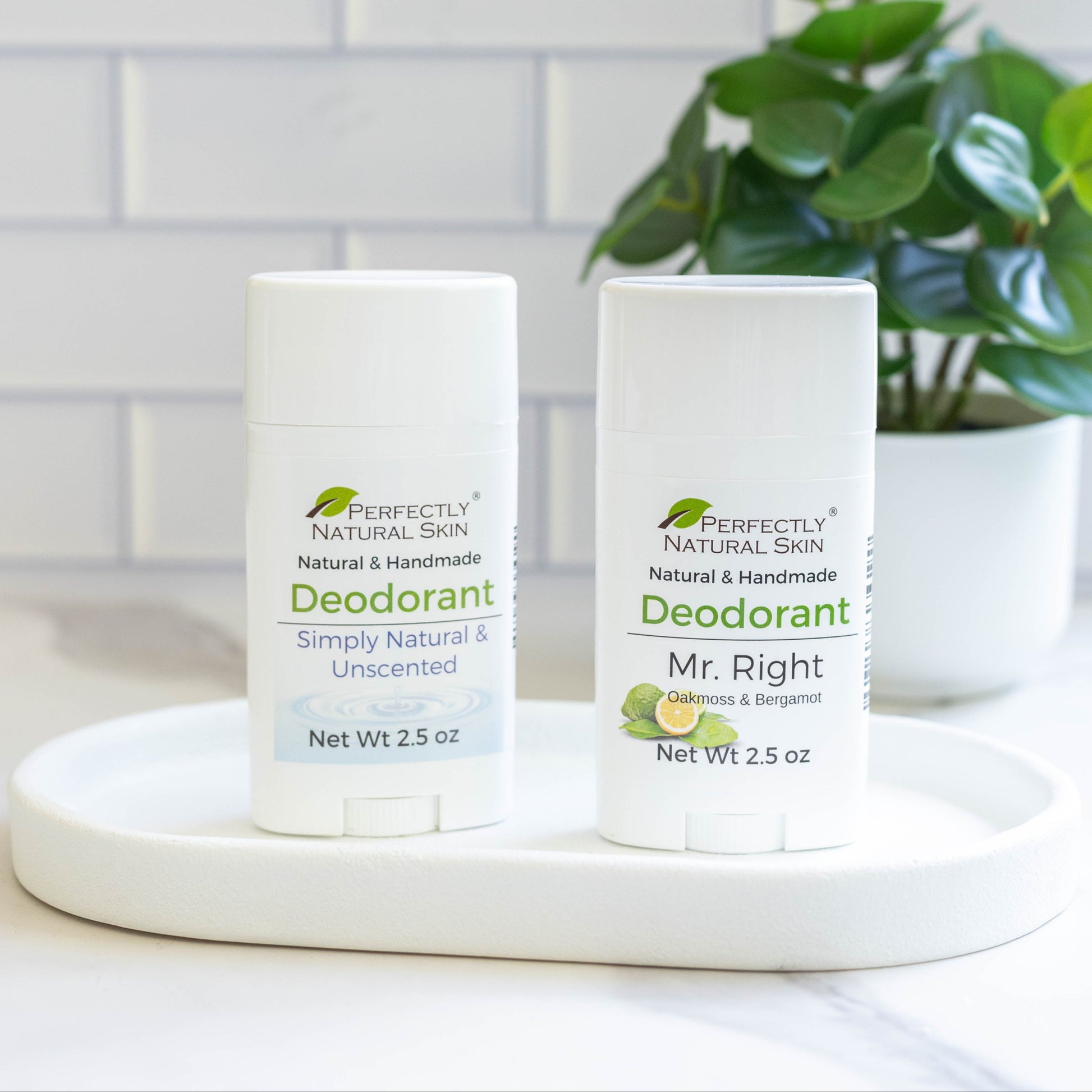 Two bottles of Perfectly Natural Skin deodorant on a white surface with a plant in the background.