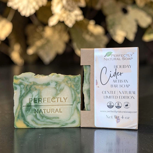 A handmade bar of soap and its packaging box from Perfectly Natural Soap, featuring a green and cream marbled design. The soap bar is embossed with 'PERFECTLY NATURAL', and the box displays 'HOLIDAY Cider Artisan Bar Soap' on a kraft paper sleeve.
