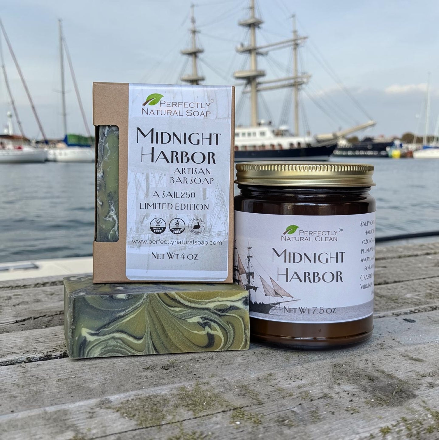 Three 'Perfectly Clean' products including a candle, soap bar, and box on a wooden dock with ships in the background.