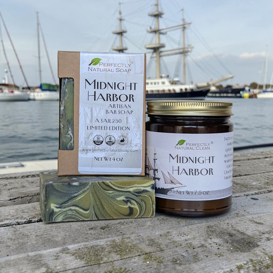 Three 'Perfectly Clean' products including a candle, soap bar, and box on a wooden dock with ships in the background.