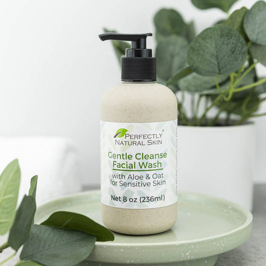A bottle of Perfectly Natural Skin Gentle Cleanse Facial Wash sits on a light green ceramic tray, styled with eucalyptus leaves and a potted plant in the background.